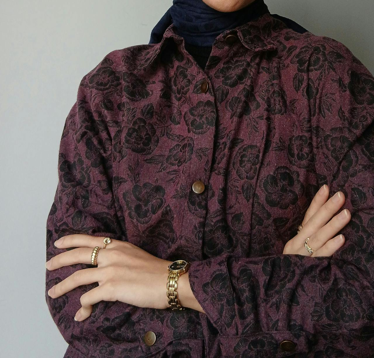 Close-up of an elegant coat with floral design, accessorized hands with jewelry.