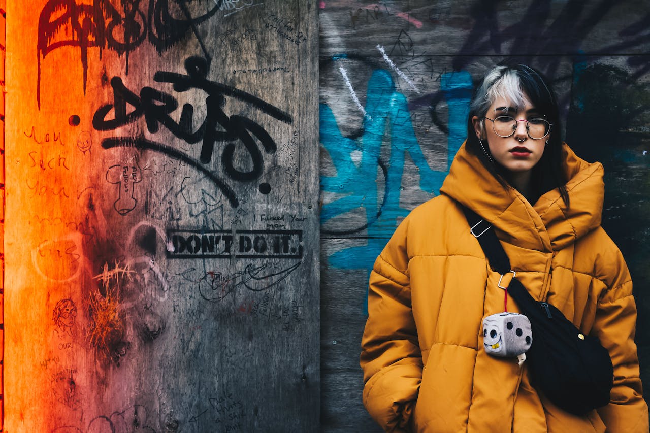 Young woman in yellow winter jacket against vibrant graffiti wall, conveying urban street style.